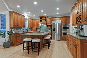 Kitchen featuring dark stone countertops, a kitchen bar, stainless steel appliances, wood finish cabinetry, and light wood-type flooring