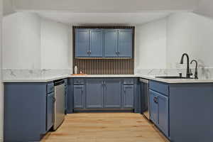 Kitchen featuring blue cabinetry, light wood-style floors, light stone countertops, and stainless steel dishwasher