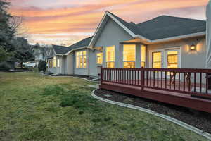Back of property featuring roof with shingles, stucco siding, a deck, and a yard