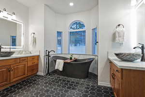 Full bathroom with two vanities, a freestanding tub, and a textured wall