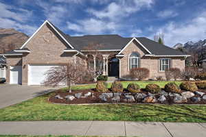 View of front of property featuring brick siding, a front yard, driveway, a mountain view, and roof with shingles