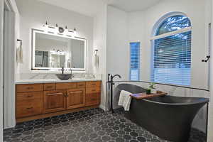 Full bath featuring vanity, a soaking tub, and a wainscoted wall