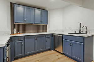 Kitchen featuring blue cabinetry, stainless steel dishwasher, and light stone counters