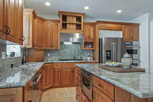 Kitchen featuring wood finish cabinets, dark stone counters, light wood-style flooring, stainless steel appliances, and backsplash