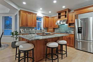 Kitchen featuring a breakfast bar, dark stone counters, stainless steel appliances, light wood-style flooring, and a kitchen island