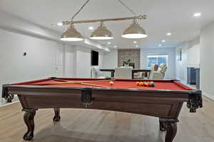 Game room with pool table, light wood finished floors, recessed lighting, and a brick fireplace
