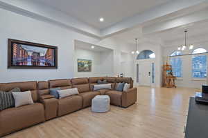 Living area featuring light wood-style floors, suspended lighting, and a high ceiling