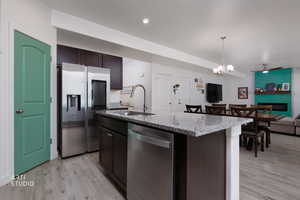 Kitchen with dark wood finish cabinetry, stainless steel appliances, a center island with sink, light stone countertops, and open floor plan