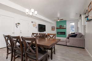 Dining space featuring a fireplace, light wood-type flooring, ceiling fan, and suspended lighting