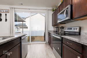 Kitchen featuring stainless steel appliances, dark wood finish cabinets, and light stone countertops