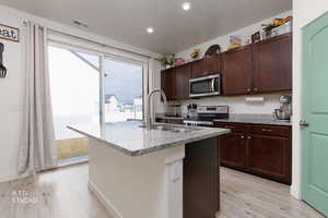 Kitchen with stainless steel appliances, light wood-style flooring, light stone counters, and an island with sink