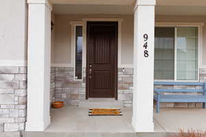Doorway to property featuring a porch, stone siding, and stucco siding