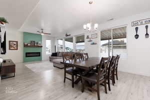 Dining room featuring a fireplace, light wood-style floors, ceiling fan, and suspended lighting
