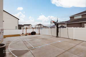 View of basketball court featuring basketball hoop, a fenced backyard, and a residential view