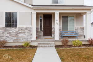 View of exterior entry featuring stone siding, covered porch, stucco siding, and a lawn
