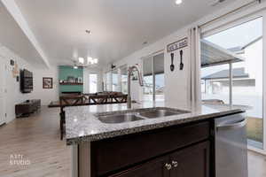 Kitchen featuring dark wood finish cabinetry, light stone countertops, light wood-type flooring, a kitchen island with sink, and hanging lights