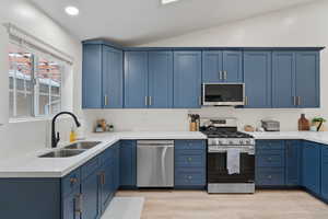 Kitchen with blue cabinetry, stainless steel appliances, light stone countertops, vaulted ceiling, and recessed lighting