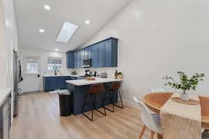Kitchen featuring blue cabinetry, a breakfast bar, a skylight, a peninsula, and light wood finished floors