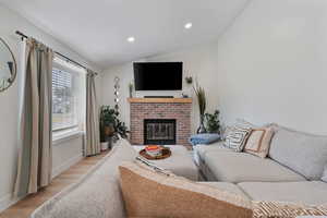 Living area with vaulted ceiling, wood finished floors, recessed lighting, and a fireplace