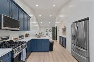 Kitchen featuring blue cabinetry, stainless steel appliances, a peninsula, lofted ceiling, and light wood-style floors