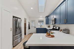 Kitchen featuring a skylight, blue cabinets, stainless steel appliances, light wood-type flooring, and a peninsula