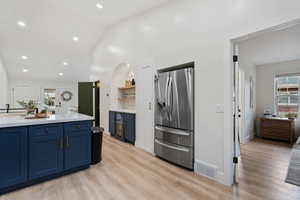 Kitchen with lofted ceiling, stainless steel refrigerator with ice dispenser, blue cabinets, light wood finished floors, and open shelves