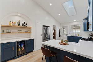 Kitchen featuring blue cabinetry, a kitchen bar, open shelves, a peninsula, and vaulted ceiling