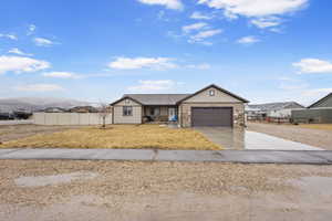 Ranch-style home featuring concrete driveway, stone siding, and an attached garage