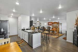 Kitchen with a peninsula, dark wood-style flooring, a kitchen bar, white cabinetry, and dark stone counters