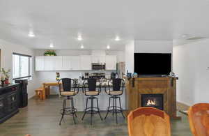 Kitchen featuring white cabinets, stainless steel appliances, a breakfast bar area, a glass covered fireplace, and dark wood-style floors