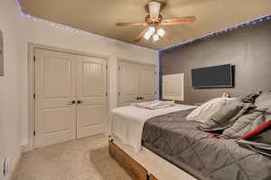 Bedroom featuring multiple closets, light colored carpet, and a ceiling fan