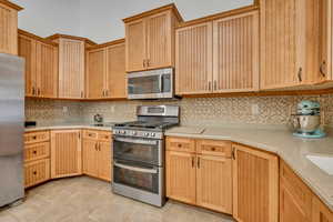 Kitchen featuring stainless steel appliances, light wood finish cabinetry, and light stone counters