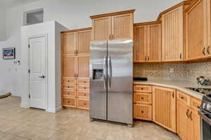 Kitchen featuring stainless steel appliances, light wood finish cabinets, decorative backsplash, and light tile patterned flooring