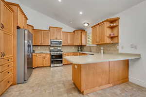 Kitchen featuring a peninsula, stainless steel appliances, lofted ceiling, open shelves, and light tile patterned flooring