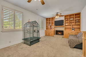 Living room featuring ceiling fan, a tile fireplace, light carpet, and built in features