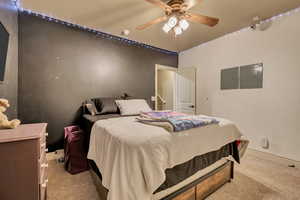 Bedroom with light colored carpet, electric panel, and ceiling fan