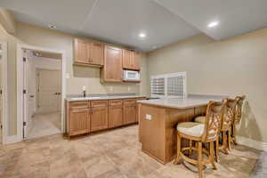 Kitchen featuring a kitchen breakfast bar, a peninsula, white microwave, recessed lighting, and light stone countertops