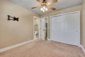 Unfurnished bedroom with light carpet, a ceiling fan, a closet, and ensuite bath