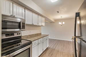 Kitchen featuring stainless steel appliances, dark stone counters, white cabinets, and tasteful backsplash