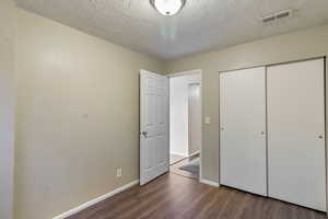 Unfurnished bedroom with dark wood-style floors, a closet, and a textured ceiling