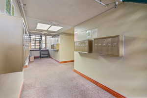 Hallway with mail area, light carpet, and a textured ceiling
