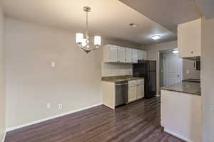 Kitchen featuring dark stone countertops, white cabinetry, a chandelier, dark wood-style floors, and tasteful backsplash