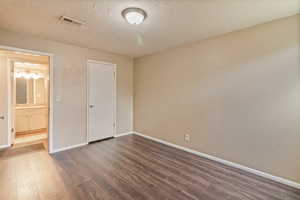 Unfurnished bedroom with dark wood-style flooring, a textured ceiling, and ensuite bathroom