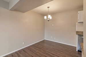 Unfurnished dining area featuring suspended lighting and dark wood-style floors