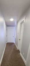 Hall with dark colored carpet and a textured ceiling