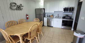 Kitchen featuring stainless steel appliances, white cabinets, wooden walls, light stone countertops, and light tile patterned floors