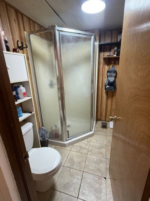 Full bathroom with wood walls, a stall shower, and light tile patterned flooring