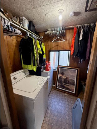 Laundry area featuring dark floors, wood walls, and washer and dryer