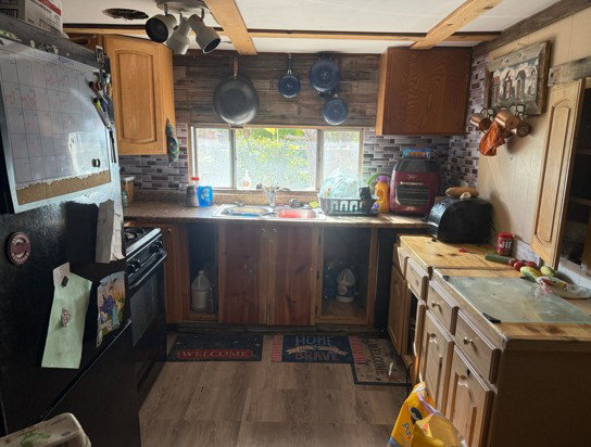 Kitchen featuring black appliances, dark wood-style flooring, beam ceiling, light countertops, and wood finish cabinetry