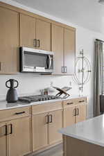 Kitchen with stainless steel appliances, light wood finish cabinetry, light wood finished floors, and light stone countertops
